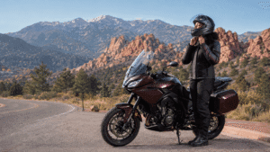 An image of a female biker standing beside their parked motorcycle outside next to a Colorado road.